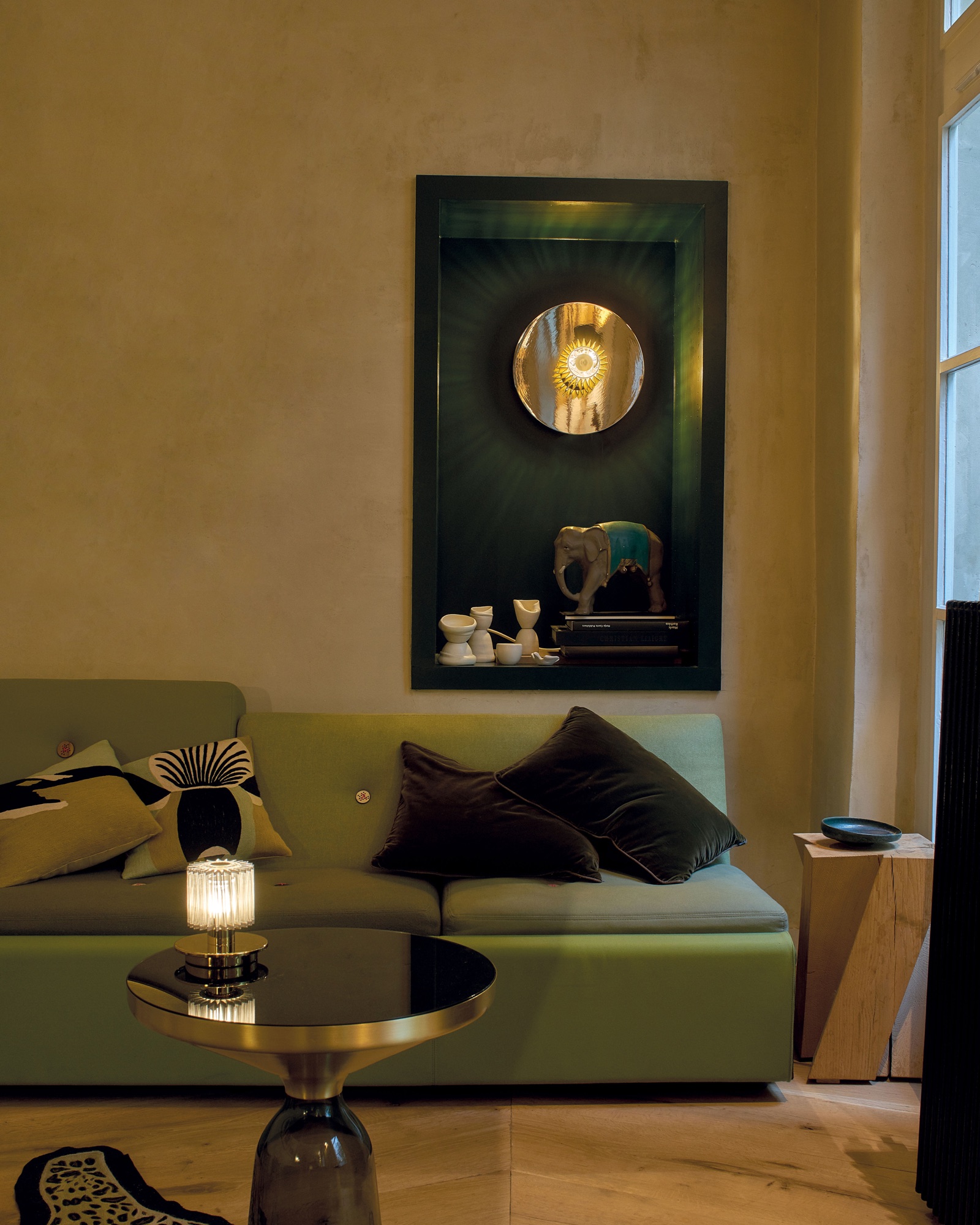 Salon de design : canapé vert, table d'appoint en laiton, lampe et niche éclairée
